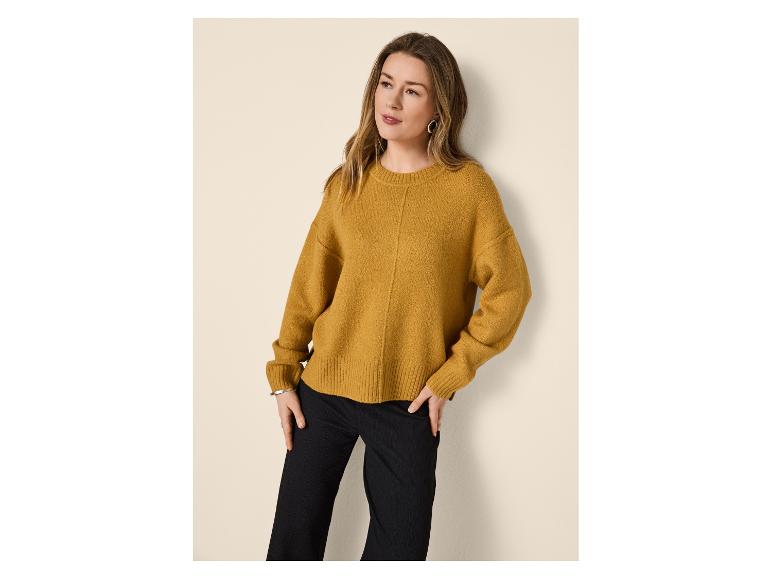 Femme portant un pull tricoté jaune moutarde et un pantalon noir, mains dans les poches