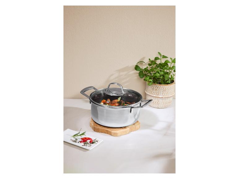 Marmite en acier inoxydable avec couvercle en verre, légumes et herbes.