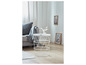 Une table basse en métal blanc avec un design tressé, à côté d'un canapé gris avec une couverture grise.