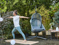 Une femme fait du yoga sur un tapis dans le jardin, à côté d'un fauteuil suspendu.