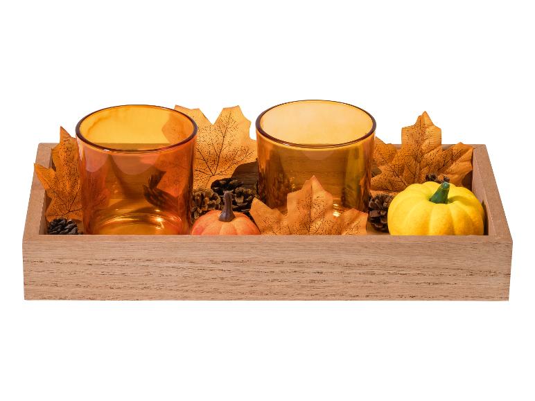 Décoration d'automne avec deux photophores orange, des feuilles, des pommes de pin et des citrouilles dans un plateau en bois.