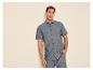Jeune homme en chemise et short en lin gris, souriant.