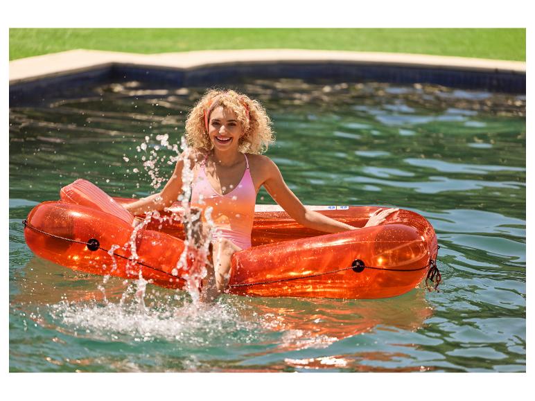 Femme souriante sur un flotteur orange transparent dans une piscine.