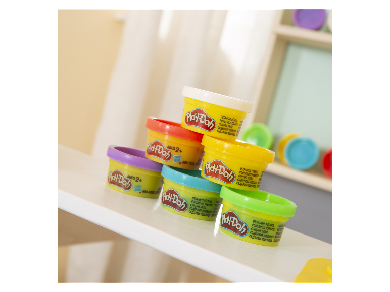 Plusieurs pots de pâte à modeler Play-Doh de couleurs différentes sur une table blanche.
