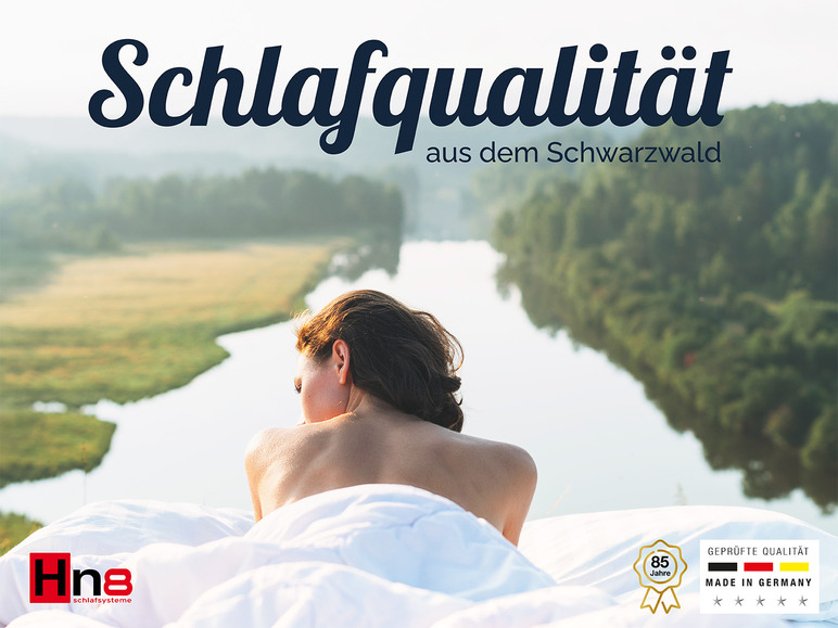 Une femme allongée sur des draps, avec une rivière et des bois en arrière-plan, publicité pour les systèmes de sommeil Hn8.
