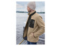 Un homme portant une veste en polaire beige avec des détails noirs, des lunettes et un bonnet gris.