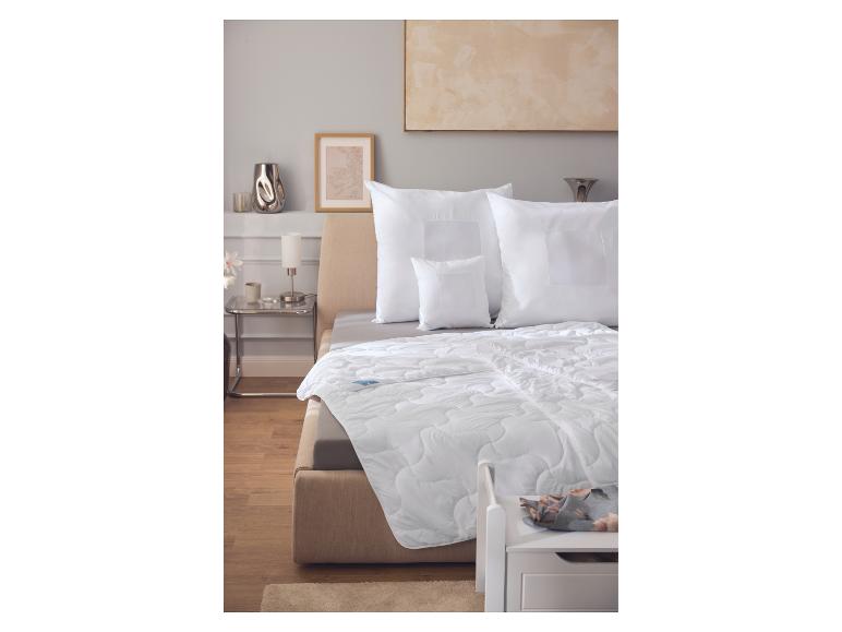 Couette et oreillers blancs sur un lit beige dans une chambre avec parquet.