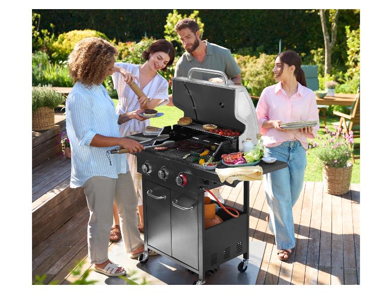 Quatre amis font griller des hamburgers et des légumes sur un barbecue à gaz Grillmeister dans un jardin.