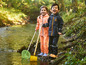 Deux enfants en imperméables avec un filet et une pelle au bord d'un ruisseau.