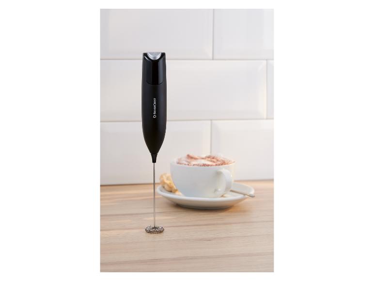 Mousseur à lait à côté d'une tasse de café avec de la mousse sur une surface en bois.