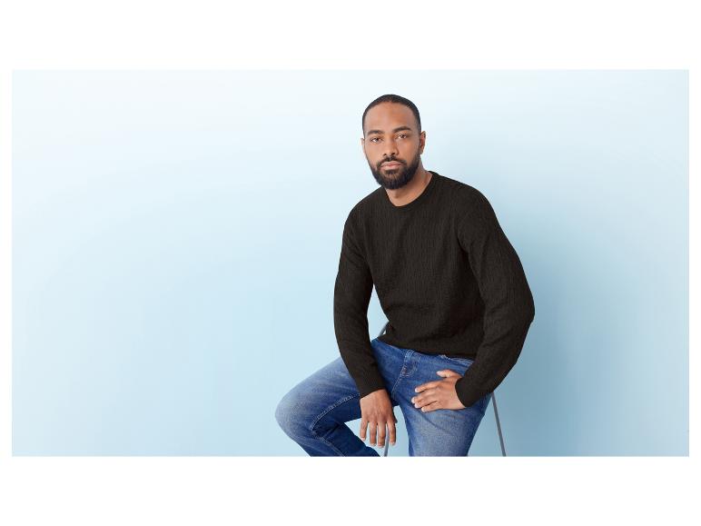 Un homme en pull noir et jean bleu.