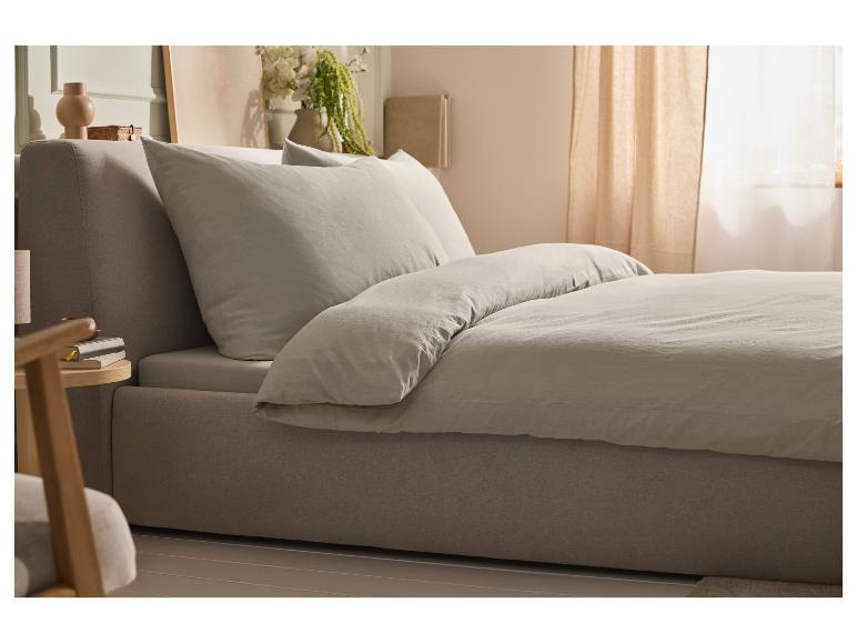 Lit avec tête de lit rembourrée et linge de lit gris clair dans une chambre lumineuse.
