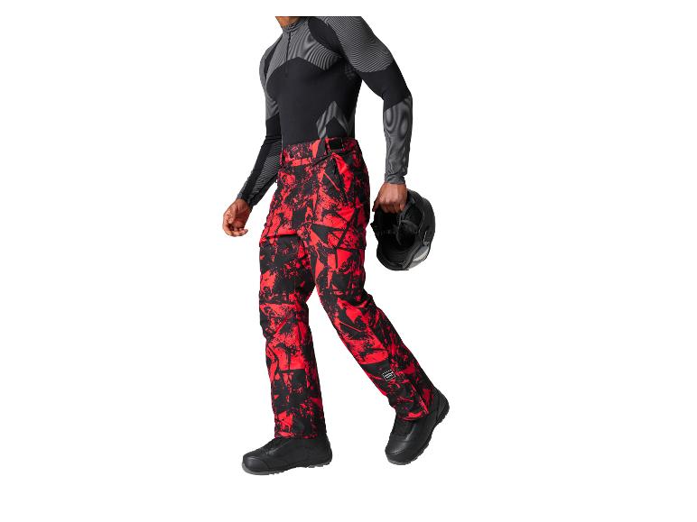 Homme en pantalon de ski rouge et noir, tenant un casque.