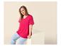 Femme en t-shirt fuchsia et jean bleu, assise sur un bloc blanc.
