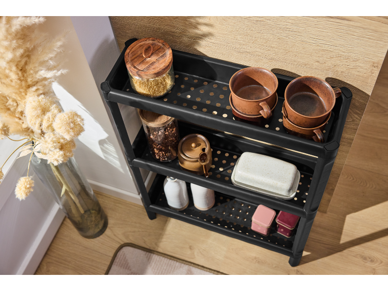 Étagère de rangement noire à 3 niveaux avec des articles de cuisine comme des bocaux, des tasses et un beurrier.