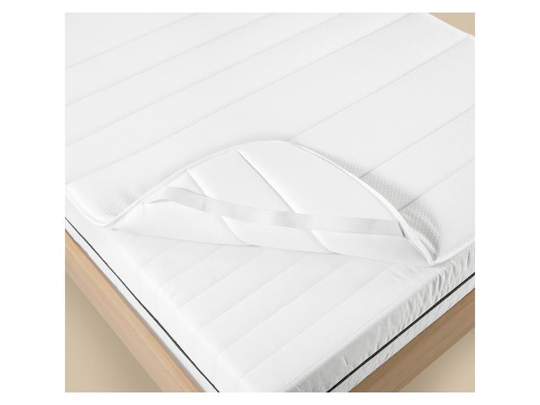 Protège-matelas blanc avec bandes élastiques sur un matelas dans un lit en bois.