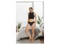 Femme en crop top et culotte noirs, debout dans une chambre avec une grande fenêtre.