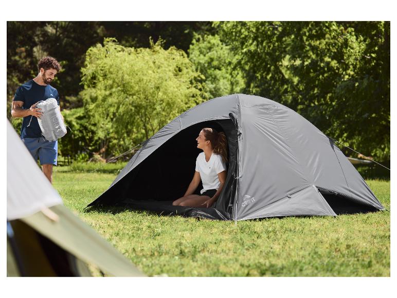 Homme avec sac de camping et femme dans une tente sur un camping herbeux.