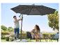 Un homme place un parasol sur une terrasse avec un salon et une carafe en verre.