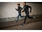 Deux coureurs en vestes de sport noires et leggings dans un tunnel.