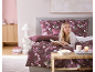 Femme lisant au lit avec une parure de lit florale bordeaux et des oreillers assortis.