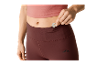 Une femme range une clé dans la poche de son legging bordeaux pour le sport.