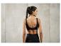 Une femme porte un soutien-gorge de sport noir et un legging devant un mur en béton.