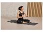 Une femme assise en position du lotus sur un tapis de yoga noir.
