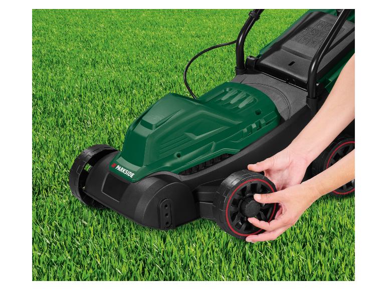 Tondeuse verte Parkside sur l'herbe, mains ajustant la roue.