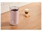 Moulin à café rose avec grains de café, un verre de café et des biscuits sur une surface en bois.