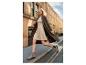 Femme en robe beige et manteau marron, courant dans une rue de la ville.