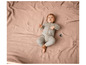 Un bébé dans une combinaison grise est allongé sur une couverture rose en tricot.