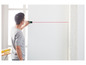 Un homme utilise un mètre laser pour projeter une ligne sur un mur blanc.