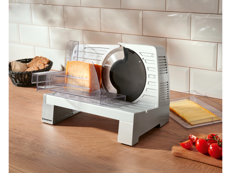 Trancheuse électrique avec fromage, pain et tomates sur un comptoir de cuisine en bois.
