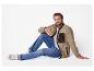 Un homme assis sur fond blanc, vêtu d'une veste polaire beige et d'un jean.