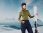 Une femme en veste et pantalon de ski tient des skis blancs devant un fond de montagnes.