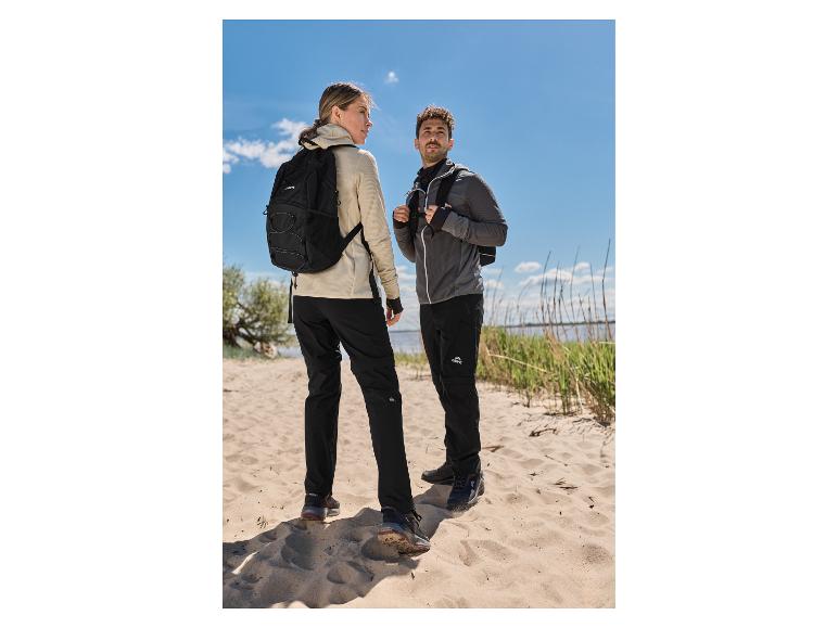 Une femme en veste technique premium beige CRIVIT et un homme en randonnée sur une plage de sable.