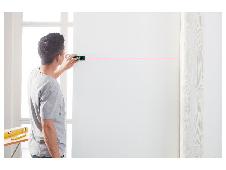 Homme utilisant un niveau laser pour projeter une ligne horizontale rouge sur un mur blanc.