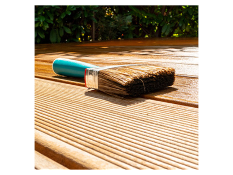 Brosse à peinture et terrasse en bois traité.