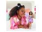 Une fille en veste rose brillante tient une poupée Barbie en robe violette.