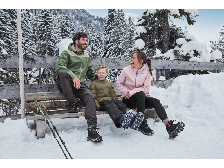 Famille en vestes et bottes d'hiver assise sur un banc dans une forêt enneigée.