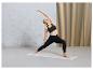 Une femme en brassière de sport et leggings noirs fait du yoga sur un tapis.