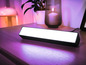 Une lumière Philips Hue noire sur une table de chevet en bois.