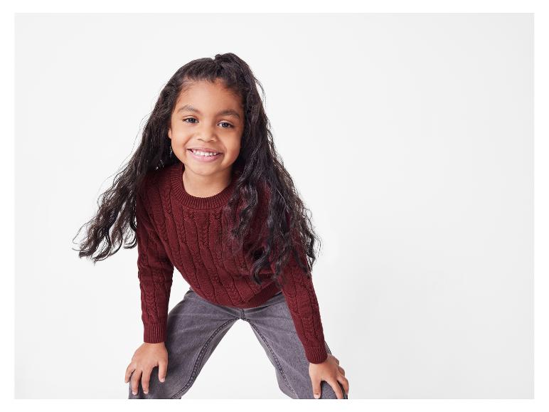 Une fille avec un pull bordeaux et un jean gris.