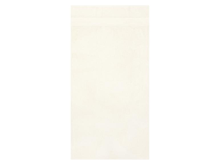 Une serviette de bain unie de couleur crème avec une bande texturée subtile près du haut.