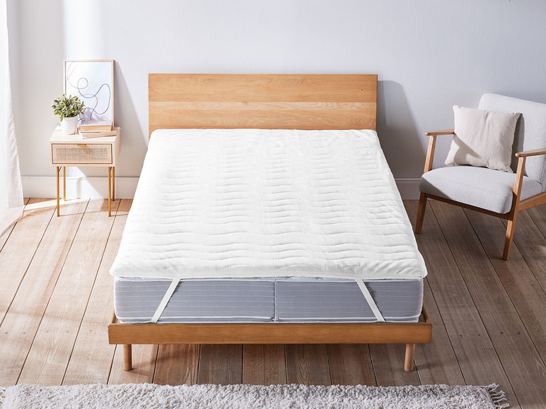 Un protège-matelas blanc sur un cadre de lit en bois.