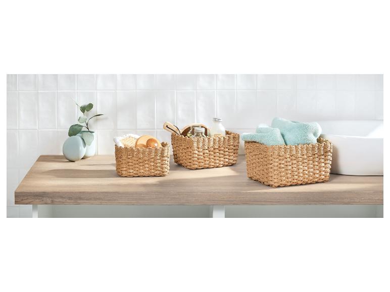 Trois paniers tressés avec accessoires de bain et serviettes sur un comptoir en bois.