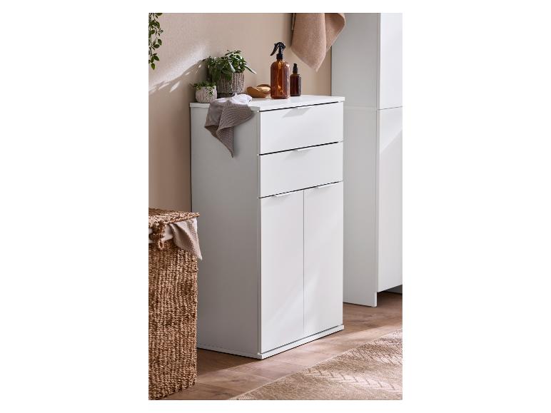 Meuble de salle de bain blanc avec tiroirs et portes, plantes et bouteilles marron dessus.