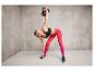 Une femme vêtue de vêtements de sport fait de l'exercice avec un kettlebell.