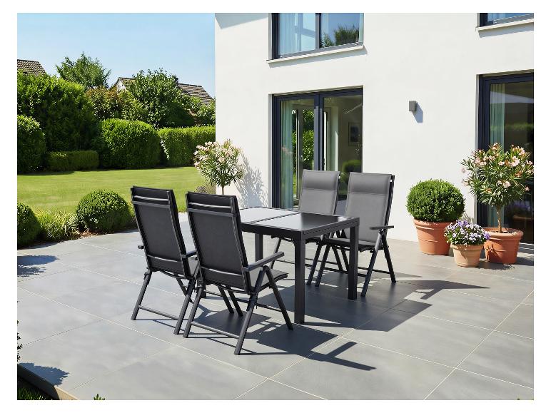 Ensemble de mobilier de jardin: table et quatre chaises sur une terrasse, entouré de verdure.